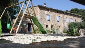 A rustic stone building with a wooden swing set and a slide in the yard. - Detached 2-bedroom apartment in charming building, swimming pool and terrace (Signes)