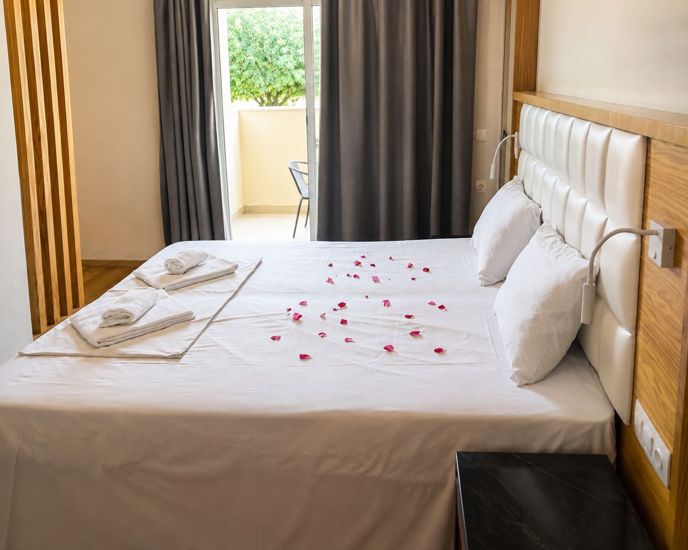 A hotel room with a bed, pillows, a bedside table, and a view of the outdoors.