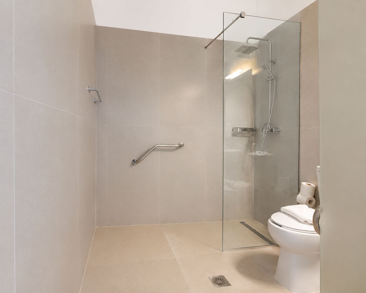 Un baño moderno con cabina de ducha de vidrio, inodoro y barra de apoyo.
