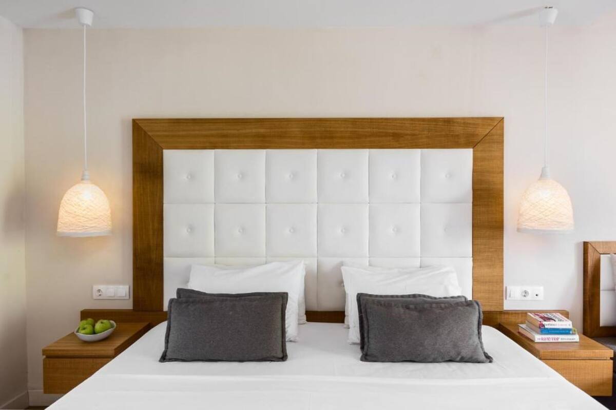 Een hotelkamer met een groot bed, twee nachtkastjes, een houten hoofdbord en hanglampen.