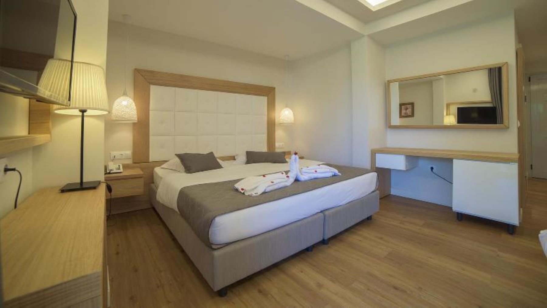 A hotel room with a bed, bedside lamps, a desk, and a mirror.