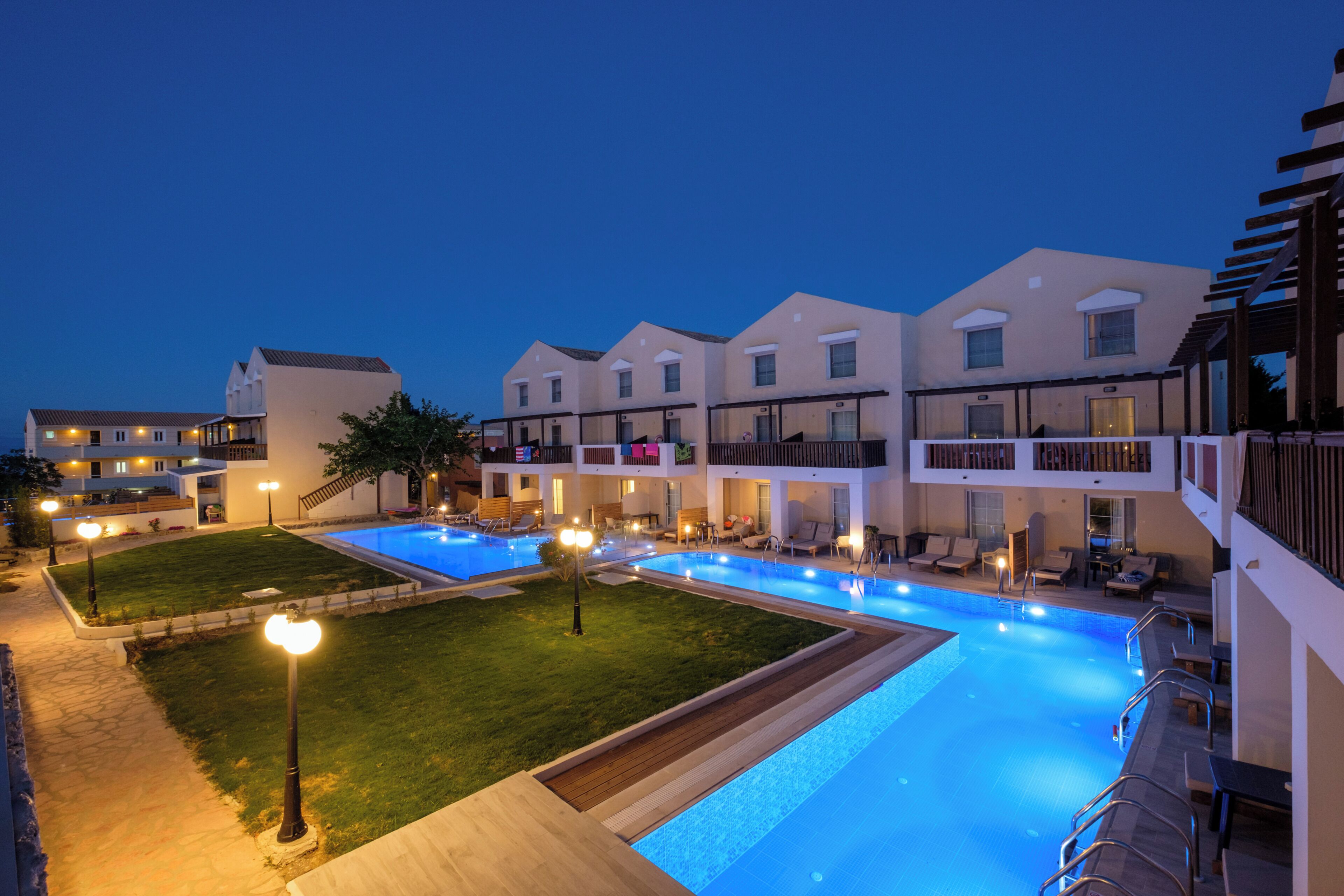 A hotel with a swimming pool, outdoor seating, and a well-lit lawn area.