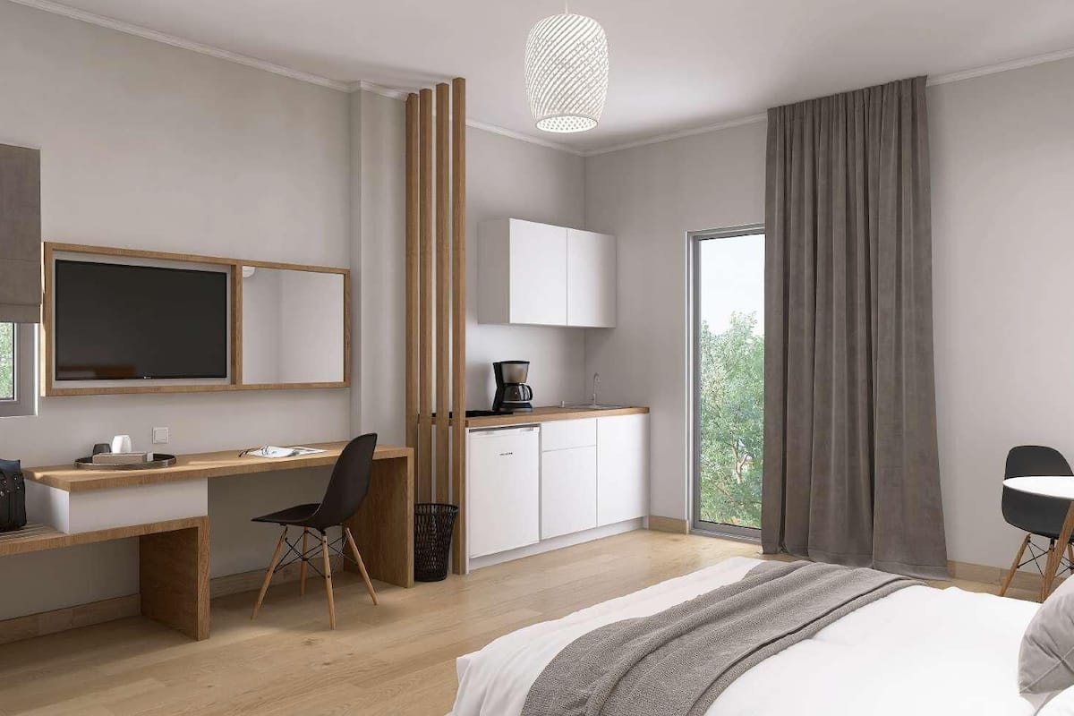 Een moderne hotelkamer met een bed, bureau, stoel en uitzicht op groen door het raam.
