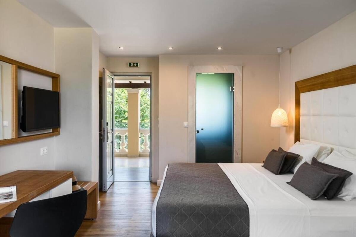 Hotelkamer met een bed, nachtkastje, stoel, televisie en een deur naar een buitenruimte.