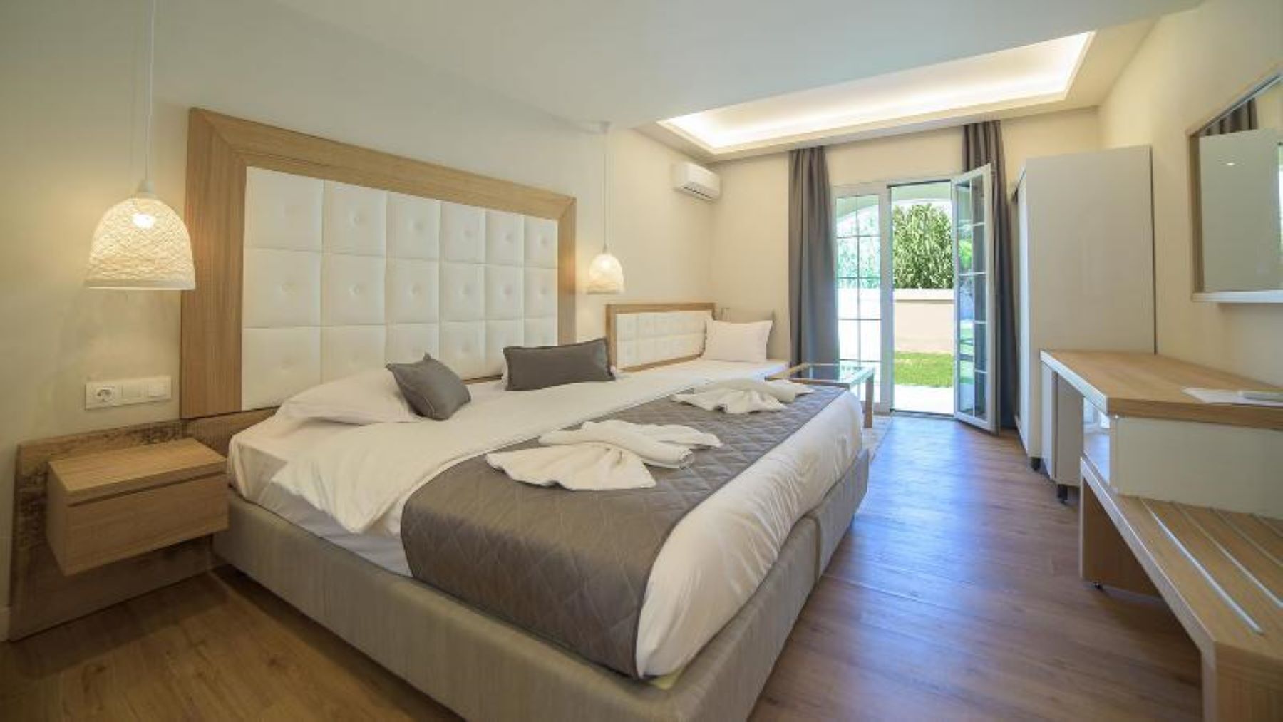 A modern hotel room with a large bed, bedside tables, a desk, and a view of the outdoors.