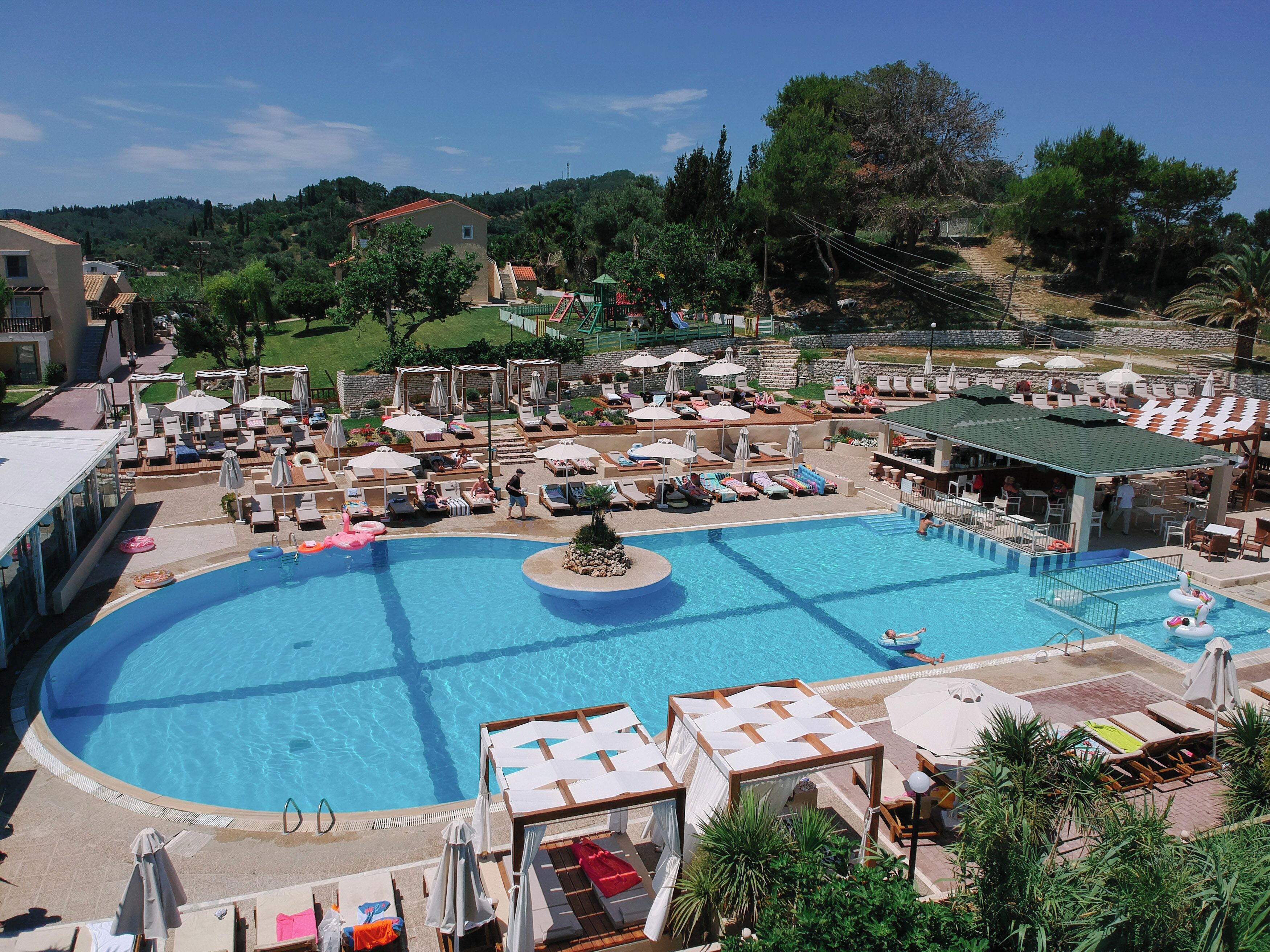 A large swimming pool surrounded by lounge chairs and umbrellas, with a view of the surrounding landscape.