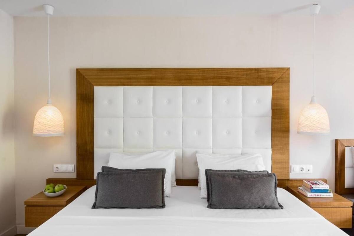 Een hotelkamer met een groot bed, twee nachtkastjes, een houten hoofdeinde en hanglampen.