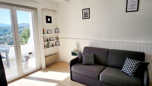 Ett vardagsrum med en grå soffa, en hund på balkongen och inramade tavlor på väggen.