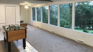 Una habitación con mesa de fútbol, ventanas amplias y ventilador de techo.