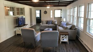 Amplia sala de estar con techo alto, ventanas grandes y televisor sobre un soporte.