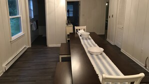 Un comedor con una larga mesa, sillas blancas y una araña.
