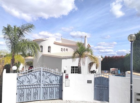 A white building with a tiled roof, a decorative metal gate, and a palm tree.