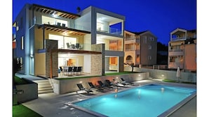 Una casa moderna de dos pisos con piscina, mobiliario exterior y fachada de piedra.