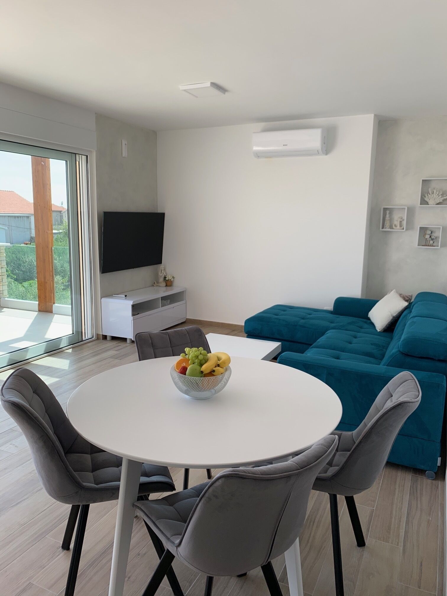 A modern living room with a blue sofa, a white dining table with chairs, and a fruit bowl.