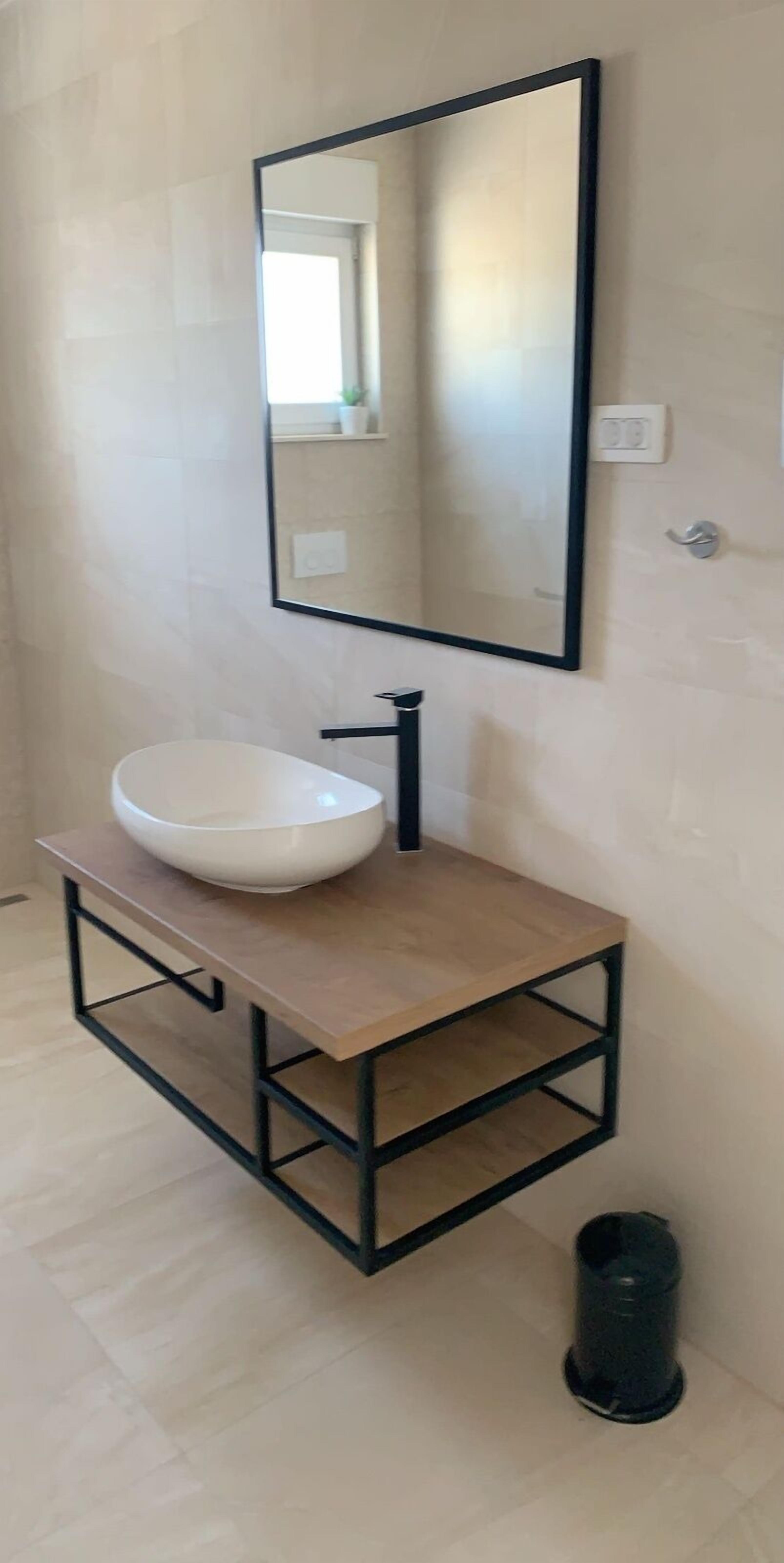 A modern bathroom with a large white sink, a black faucet, and a rectangular mirror with a black frame.