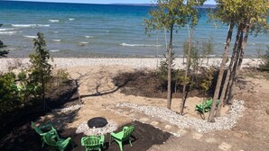 A beach with a fire pit, green chairs, and trees.