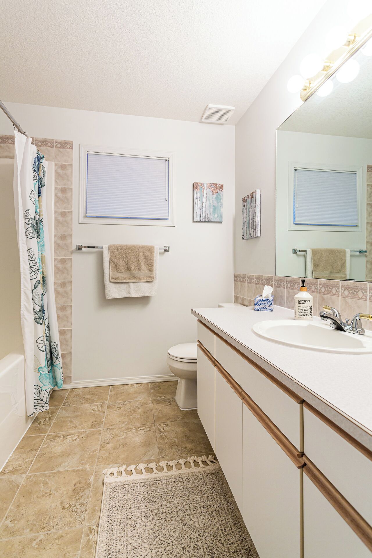 A bathroom with a bathtub, toilet, and sink. There are towels hanging on the wall, a shower curtain, and a mirror above the sink.