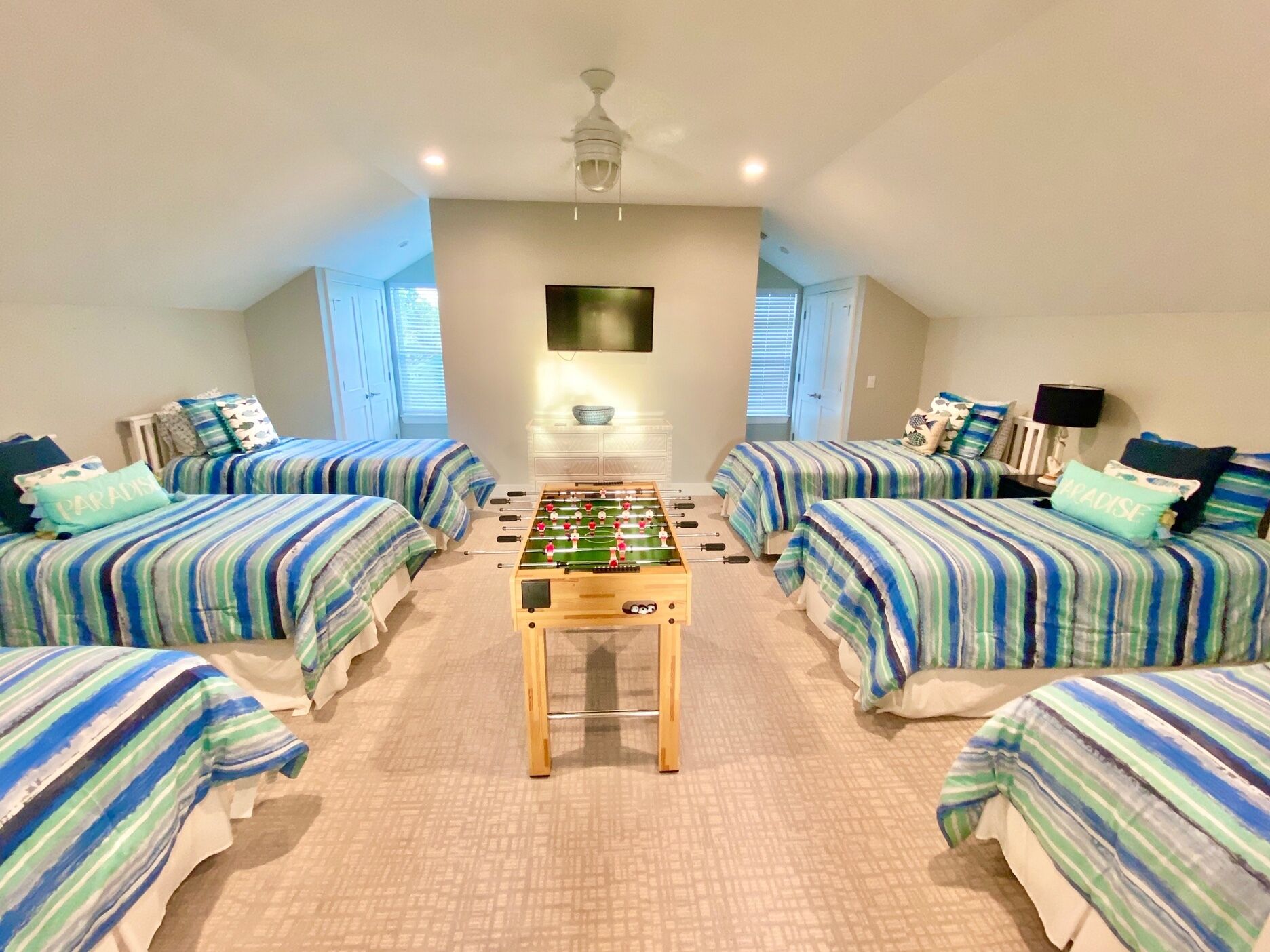 A room with four beds, a foosball table, and a TV.
