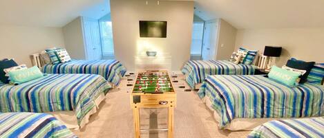 A room with four beds, a foosball table, and a TV.
