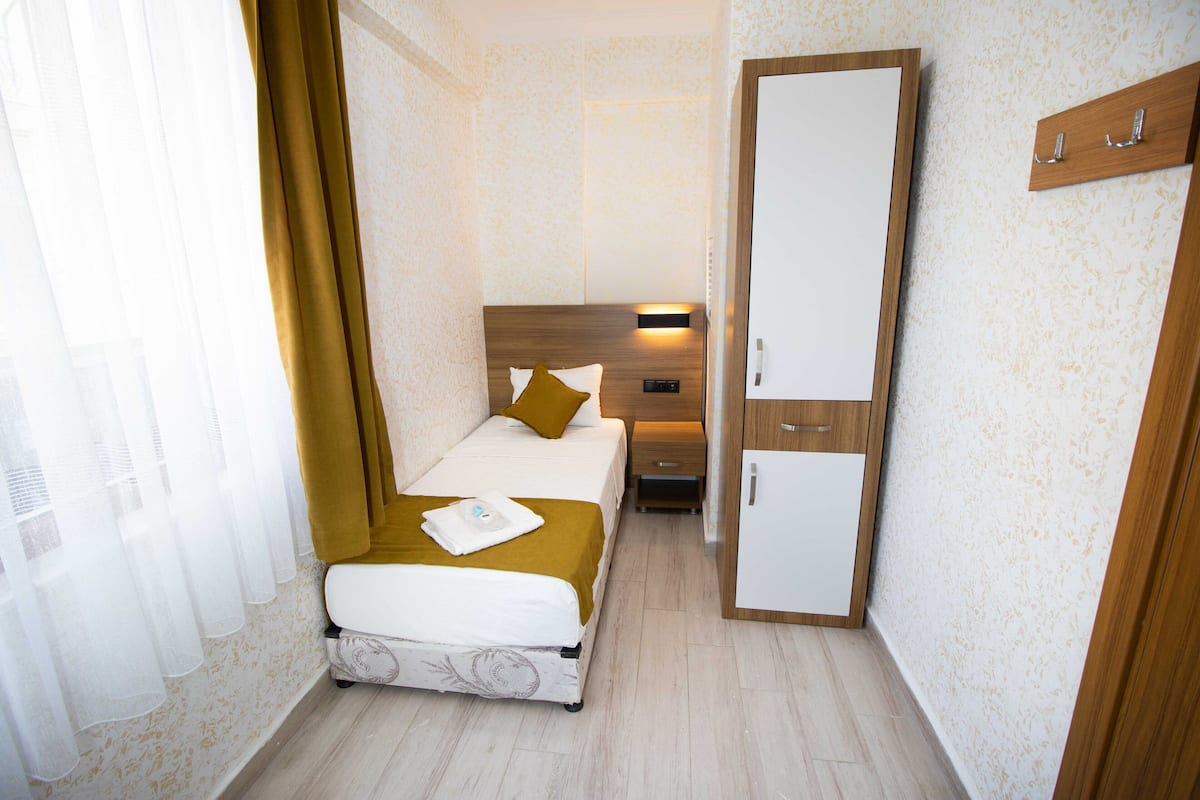 A bedroom with a bed, a nightstand, a wardrobe, and a window with sheer curtains.