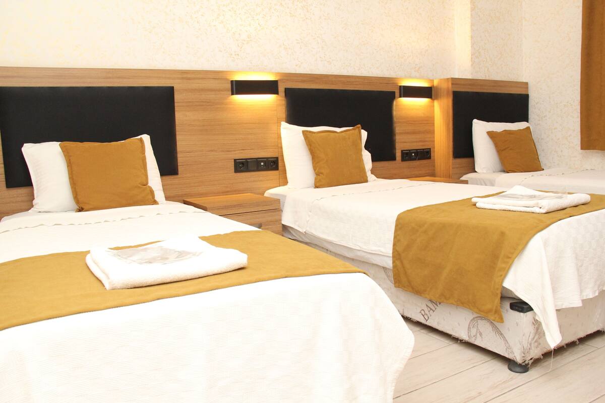 A hotel room with three beds, each with a white bedspread and a brown throw blanket.