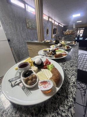 A breakfast buffet with various food items and condiments on plates, set on a granite countertop in a room with a tiled wall and a window. - Ersoy Ikiz Otel (Antalya)