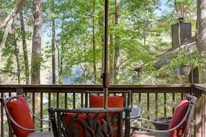 A wooden deck with metal chairs and a table, surrounded by trees.