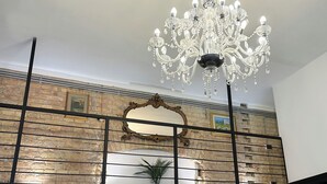 A chandelier hanging from the ceiling, a large ornate mirror, and a brick wall with a plant.