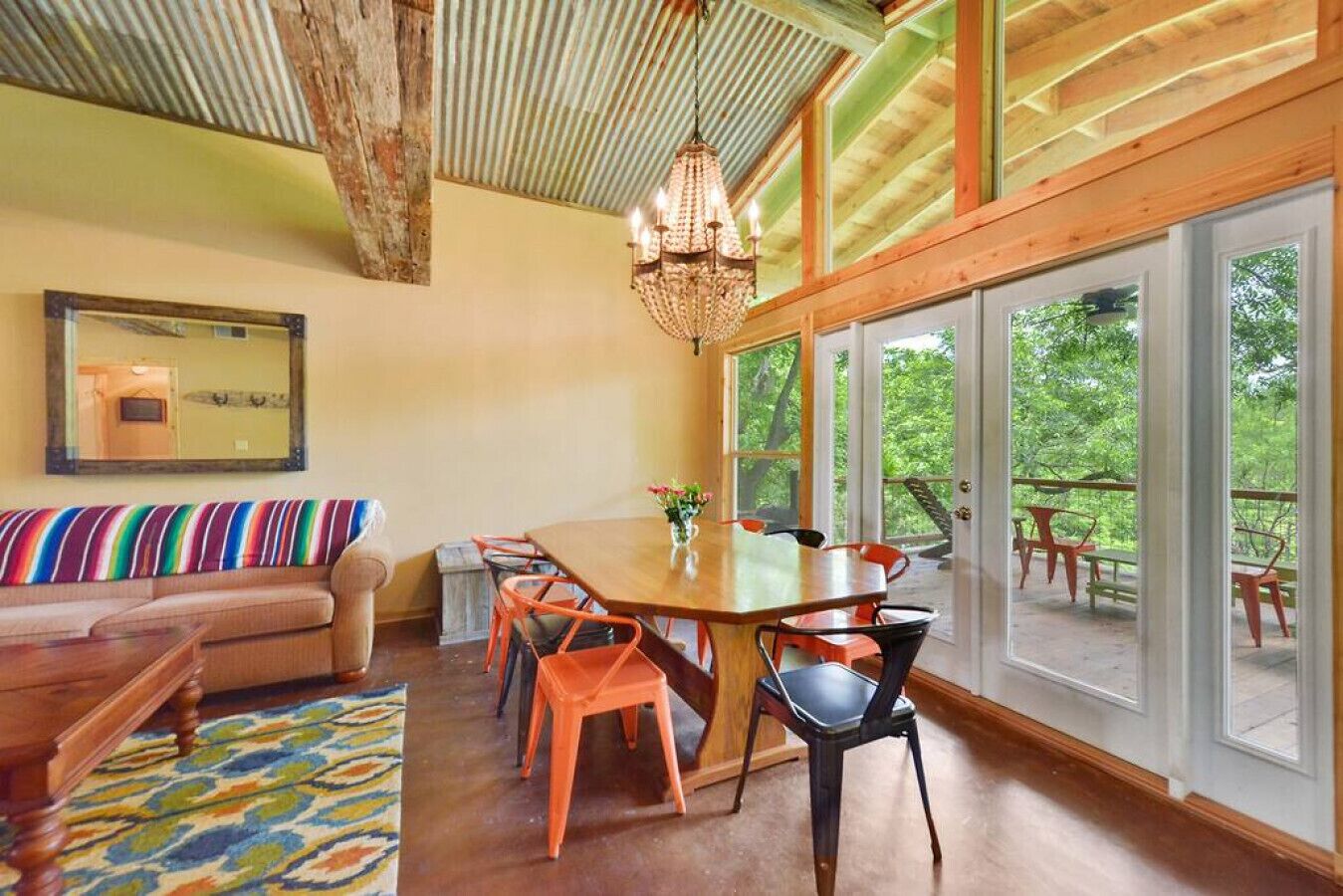 Un espace repas comprenant une table et des chaises en bois, un lustre et de grandes fenêtres donnant sur l’extérieur.