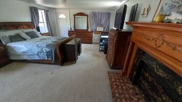 A bedroom with a bed, dresser, mirror, and fireplace.