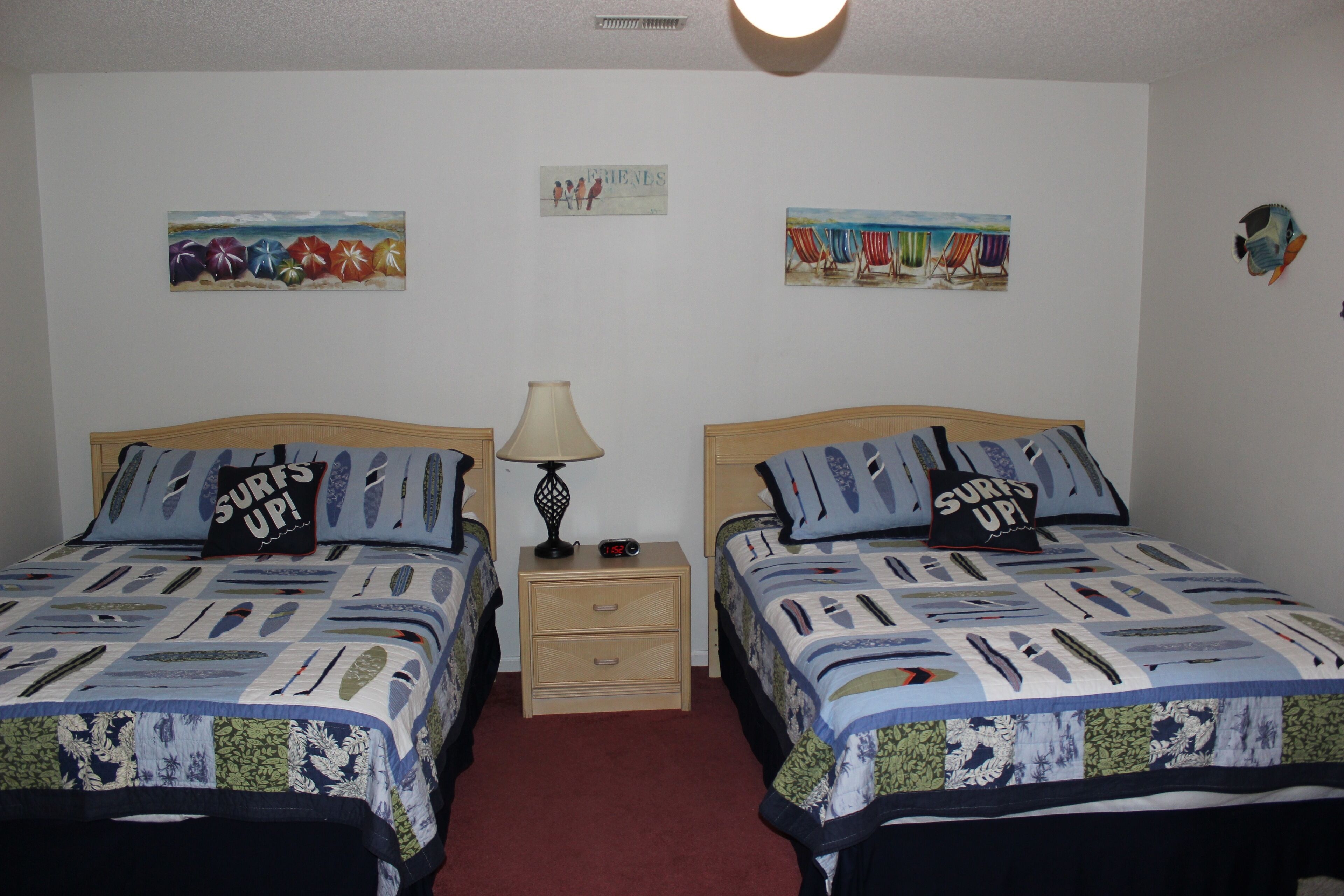 Habitación doble con dos camas, cada una con almohada de temática surf, una mesita de noche con lámpara y obras de arte en las paredes.