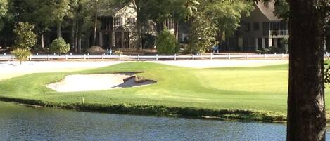 A golf course with a water hazard, trees, and a building in the background.