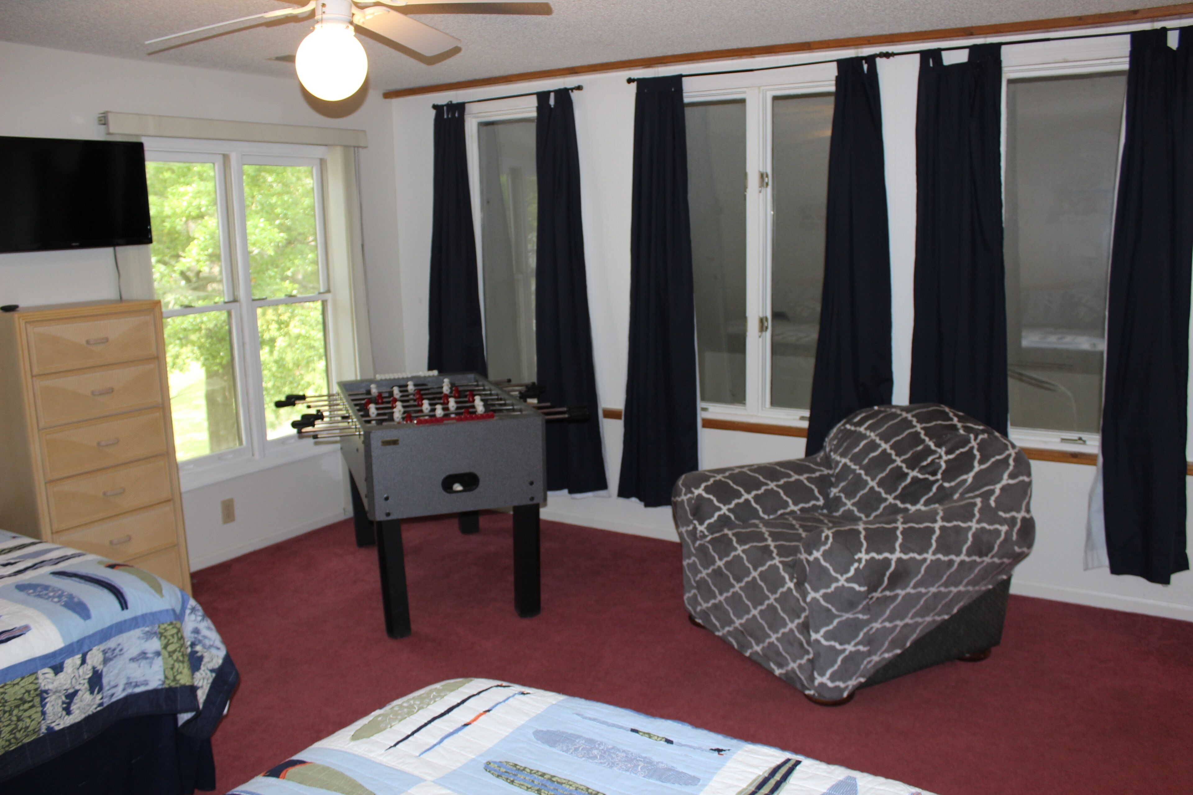 A room with a foosball table, a sofa, a bed, a dresser, and a TV mounted on the wall.