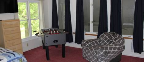 A room with a foosball table, a sofa, a bed, a dresser, and a TV mounted on the wall.