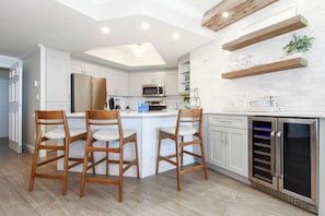 A modern kitchen with white cabinetry, a central island with bar stools, a built-in oven, and a wine fridge.