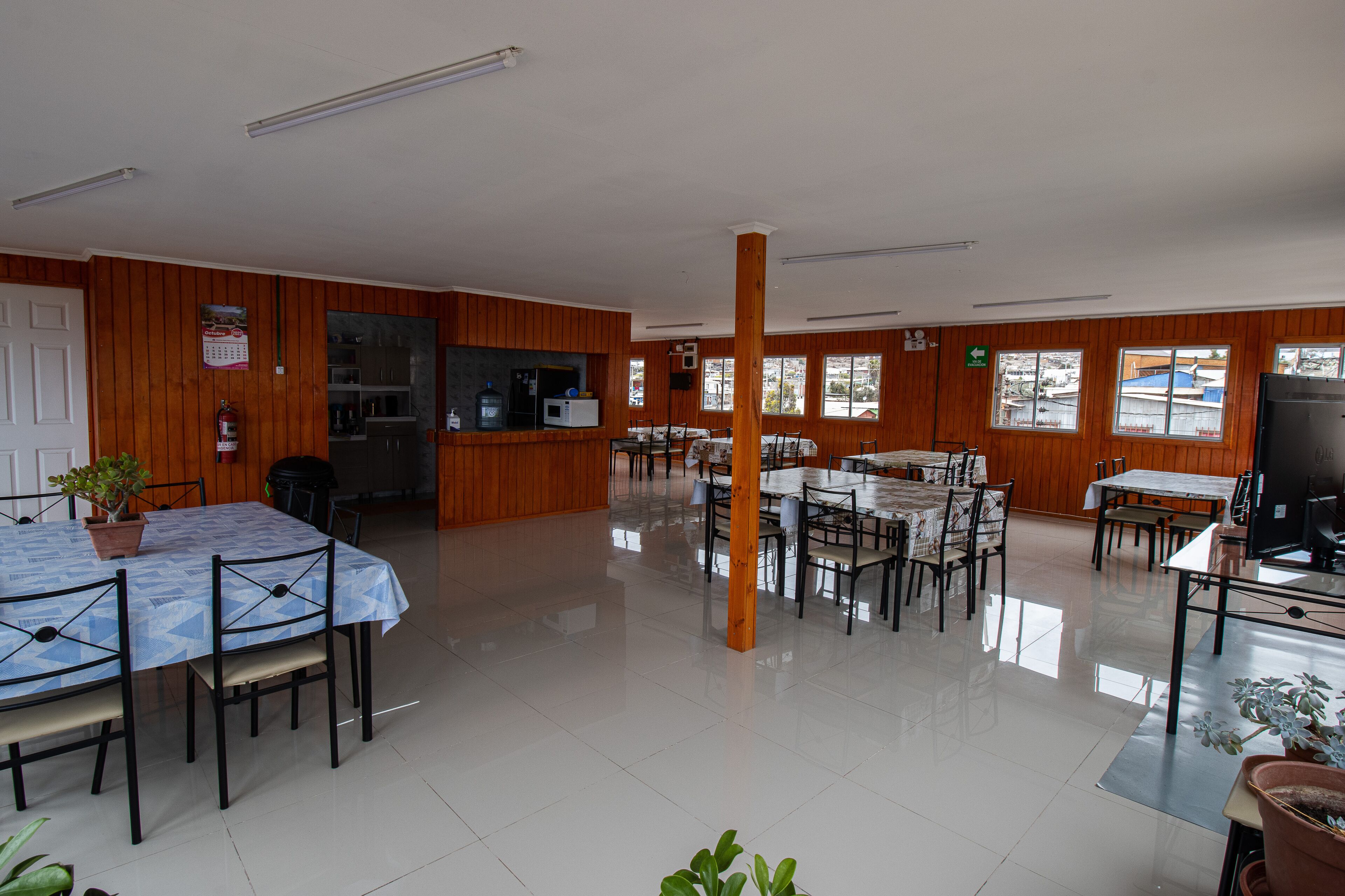 A spacious dining area with multiple tables and chairs, wooden paneling on the walls, and large windows allowing natural light.