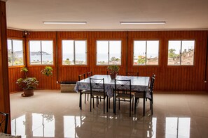 A dining area with a table and chairs, large windows with a view of the sea, and wooden paneling on the walls.