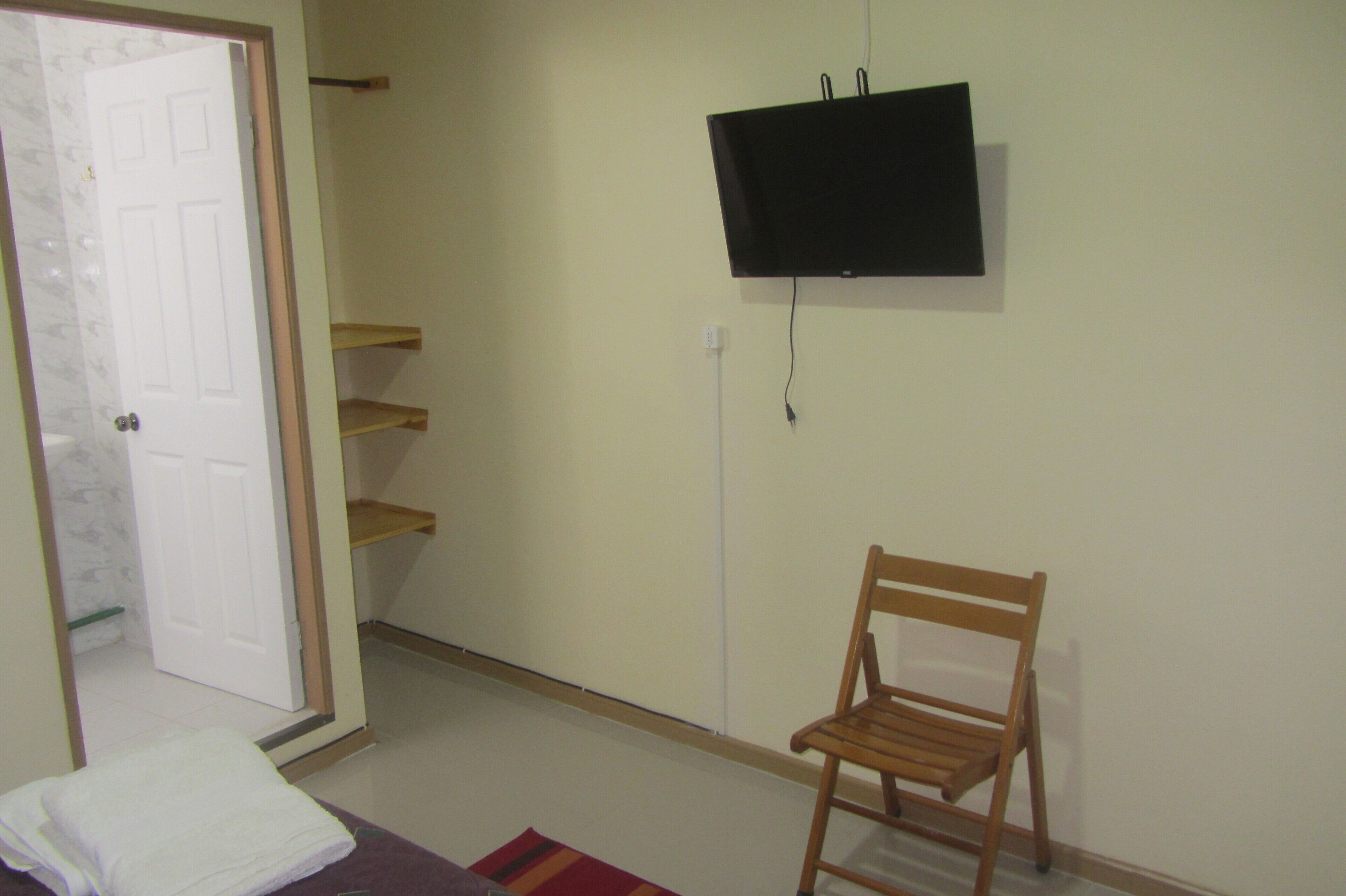 A room with a wooden chair, a television mounted on the wall, and a white door.