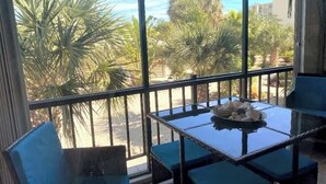 En balkon med et glasbord og stole, der giver udsigt til palmer og en gade.