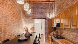 A kitchen with brick walls, wooden cabinets, a long dining table, and pendant lighting. - LUXURY HISTORIC APARTMENT (Roma)