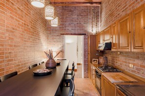 A kitchen with brick walls, wooden cabinets, a long dining table, and pendant lighting.