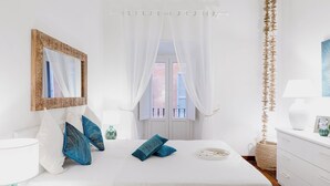 A bedroom with a bed, a bedside table, a mirror, a window with curtains, and a view of the outside. - LUXURY HISTORIC APARTMENT (Roma)