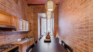 A narrow kitchen with brick walls, wooden cabinets, a long dining table, and a hanging light fixture. - LUXURY HISTORIC APARTMENT (Roma)