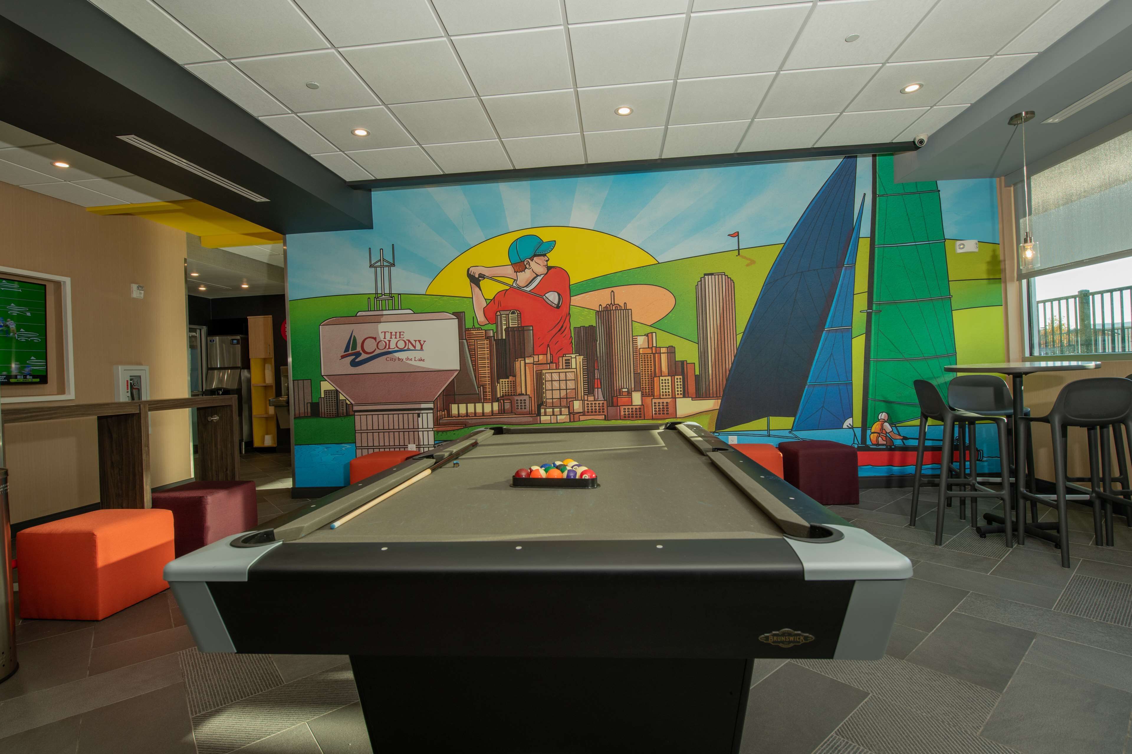 A pool table with a cityscape mural, a bar area, and orange seating.