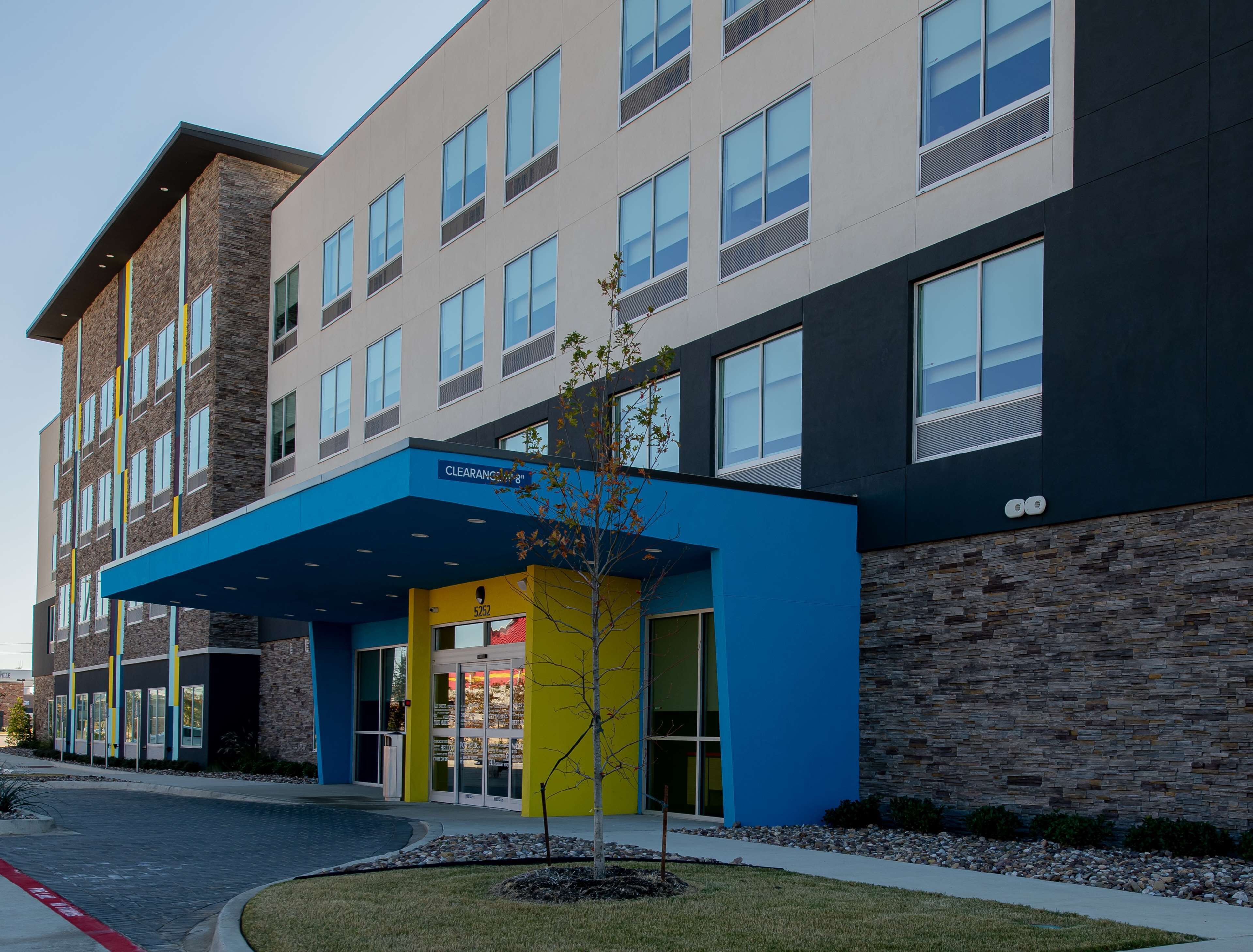 A multi-story building with a blue entrance canopy, stone facade, and multiple windows.