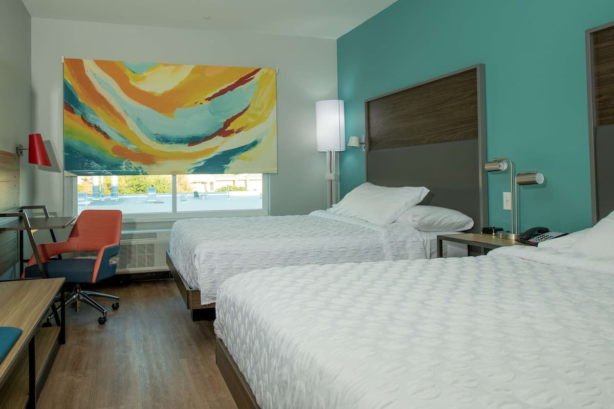 A hotel room with two beds, a desk, a chair, and a large abstract painting.