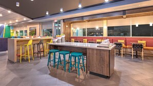 A modern restaurant with a central bar area, high stools, and a seating area with tables and chairs. - Tru by Hilton The Colony Dallas (The Colony)