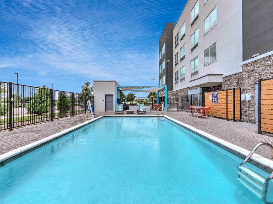 A swimming pool with a clear blue water, surrounded by a fence, and adjacent to a building with a signboard.