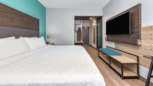 A modern hotel room with a large bed, a bench, a TV mounted on the wall, and a shower area visible through an open door. - Tru by Hilton The Colony Dallas (The Colony)
