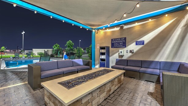 An outdoor lounge area with seating and a pool in the background. - Tru by Hilton The Colony Dallas (The Colony)